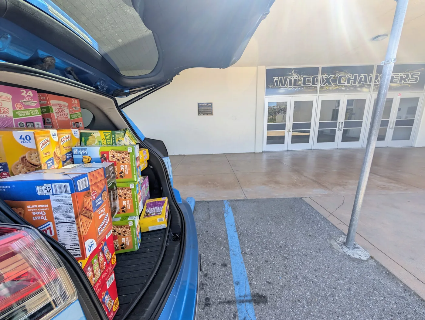A car loaded with snacks parked at the entrance to Wilcox High School, beneath the &lsquo;Wilcox Chargers&rsquo; sign.